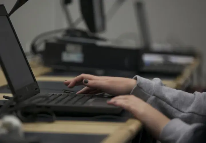 Dłonie piszą na klawiaturze laptopa, jakby śledziły coś w internecie.