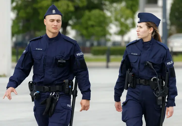 Dwóch policjantów w granatowych mundurach, z widocznymi stopniami w policji, idzie obok siebie.
