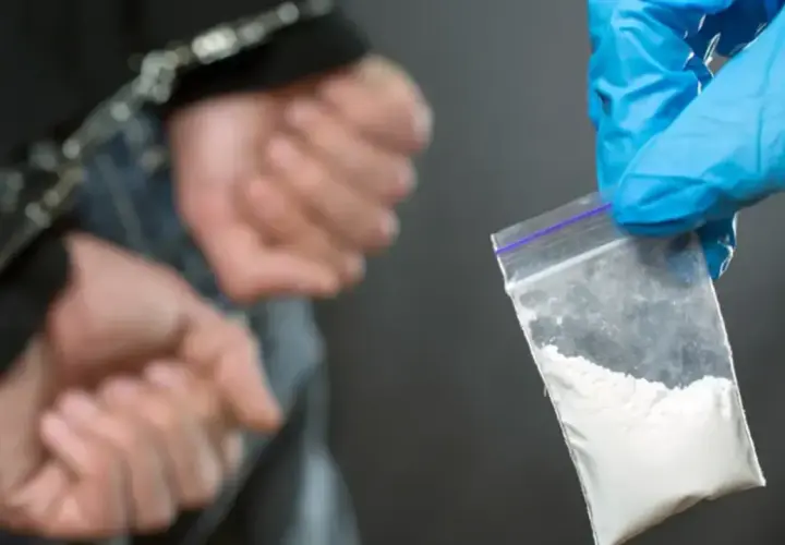 Ręce w kajdankach, obok woreczek z białym proszkiem, prawdopodobnie klefedron.