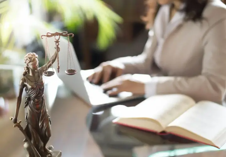 Figurka Temidy z wagą i mieczem, obok otwarta księga i osoba pracująca przy laptopie. Symbol sprawiedliwości i abolicji.