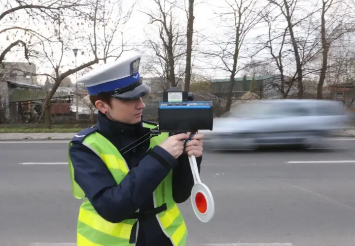 Policjantka w kamizelce odblaskowej mierzy prędkość przejeżdżającego samochodu radarem.