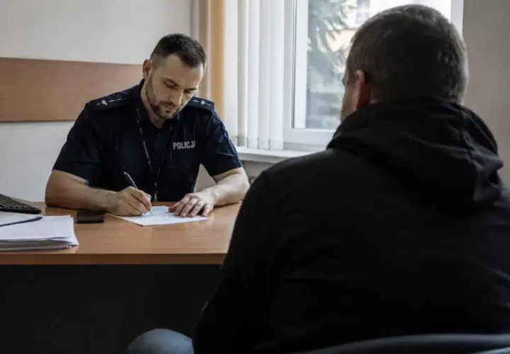 Policjant spisuje zeznania podejrzanego w pokoju przesłuchań.