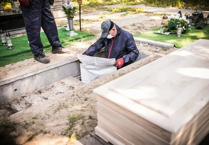 Pracownicy cmentarza przeprowadzają ekshumację, wyciągając biały worek z grobu. Obok leży drewniana trumna.