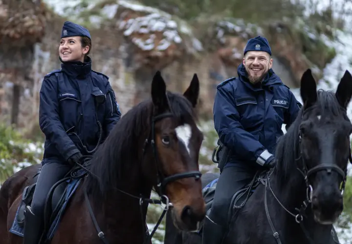 Policjanci na koniach, w tym przełożony, patrolują zimowy teren.