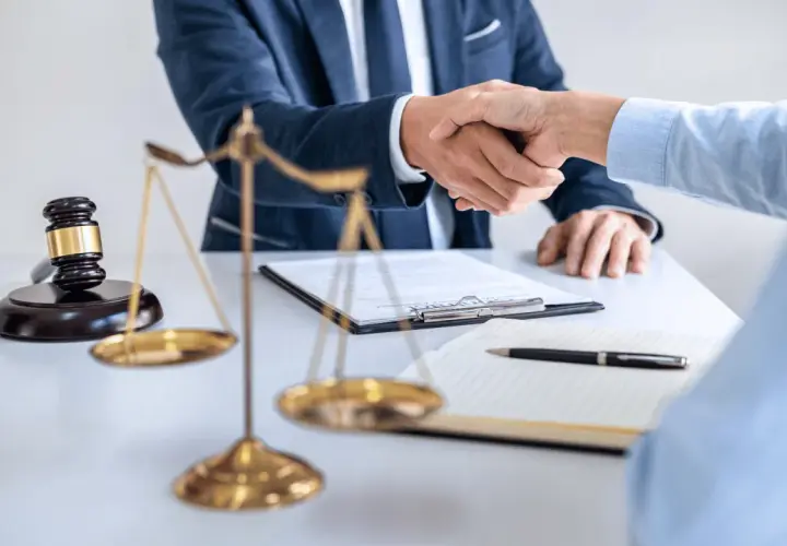 Uścisk dłoni prawników przy biurku z wagą sprawiedliwości i młotkiem. Sprawa 157 kk zakończona sukcesem.