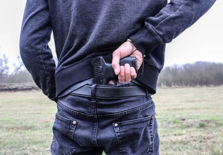 Mężczyzna chowa pistolet za pasem, gotowy do egzekwowania haraczu.