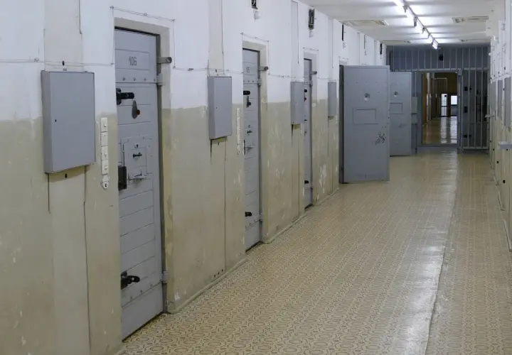 Korytarz więzienny z celami po obu stronach. Na drzwiach jednej z cel widnieje numer 106. W tle kraty i kolejne drzwi.