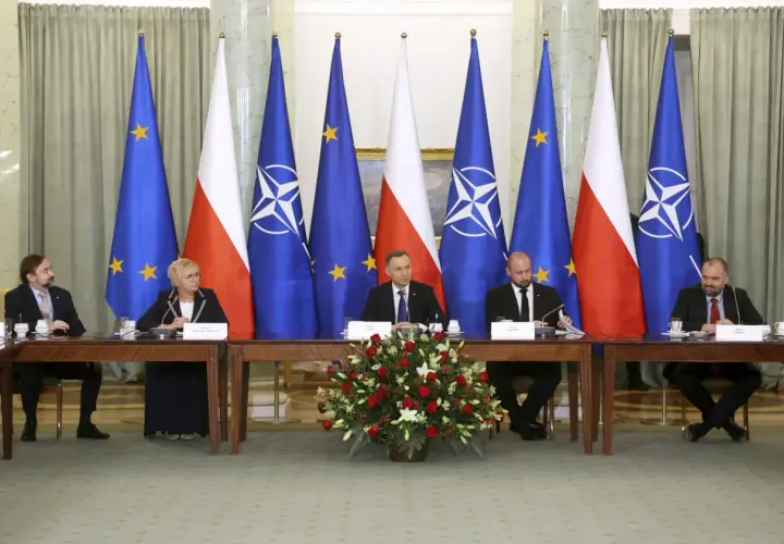 Spotkanie przy stole z flagami Polski, UE i NATO. Dyskusja o bezpieczeństwie i artykuł 5 NATO.