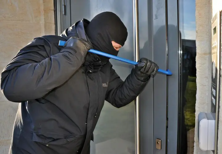 Złodziej w kominiarce i rękawiczkach próbuje wyważyć drzwi łomem. To może być próba włamania, zgodnie z art. 279 kk.