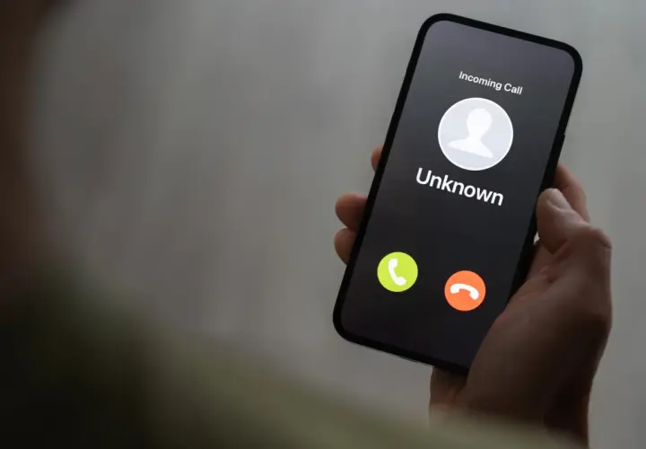 Dłoń trzyma smartfon z ekranem blokady, na którym widnieje "Incoming Call" od nieznanego numeru. Uważaj na vishing!