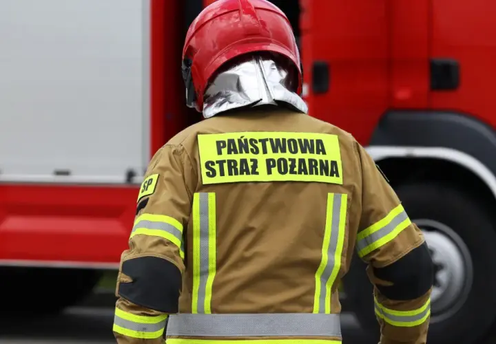 Strażak w hełmie i kurtce z napisem "Państwowa Straż Pożarna" gotowy do akcji. Alarm bombowy? Nie, to tylko ćwiczenia.