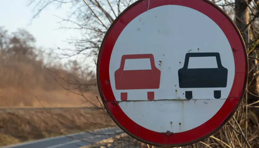 Znak drogowy zakaz wyprzedzania. Czerwony samochód z przodu, czarny z tyłu.