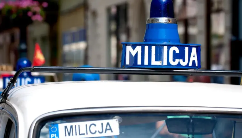 Niebieska lampa i napis "MILICJA" na dachu białego samochodu.