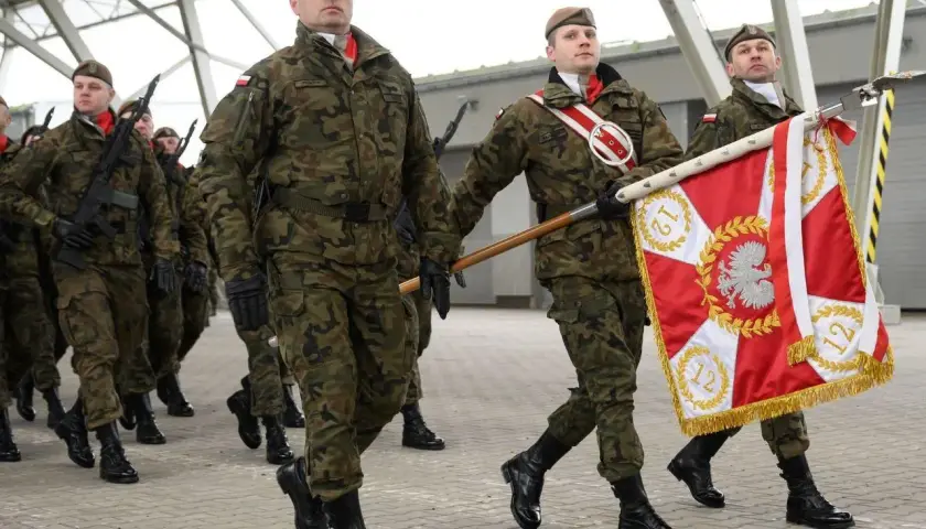 Żołnierze w mundurach maszerują z flagą. Uroczysta przysięga wojskowa w pełnym rynsztunku.