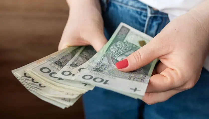 Dłonie trzymające stos banknotów 100 zł. Czy to przyszła kwota bazowa służba cywilna 2026?