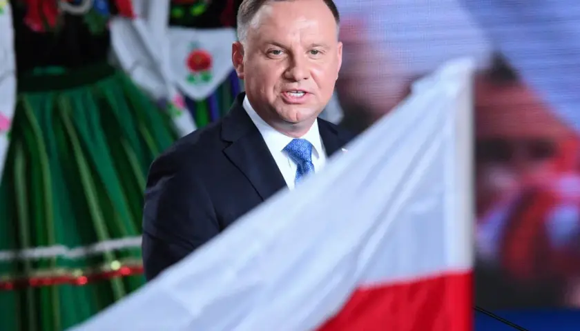 Prezydent Andrzej Duda z polską flagą, w tle ludowy strój. Może to symbolizować ułaskawienie i dumę narodową.