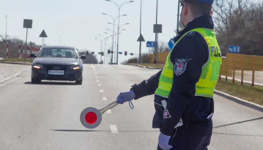 Policjant kieruje ruchem, egzekwując przepisy ruchu drogowego. Na drodze stoi samochód.