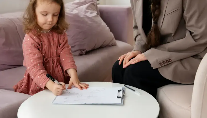 Mała dziewczynka rysuje, a obok siedzi kurator.