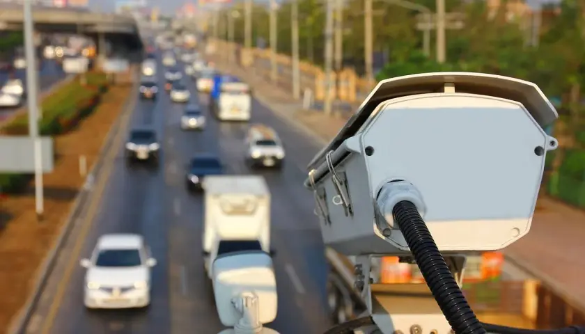 Kamera monitorująca ruch drogowy. Czy policja może wykryć antyradar? Zbliżenie na białą kamerę z kablem, w tle ruchliwa autostrada.