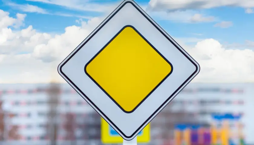 Znak droga z pierwszeństwem. Na tle błękitnego nieba z chmurami, biały romb z żółtym środkiem.