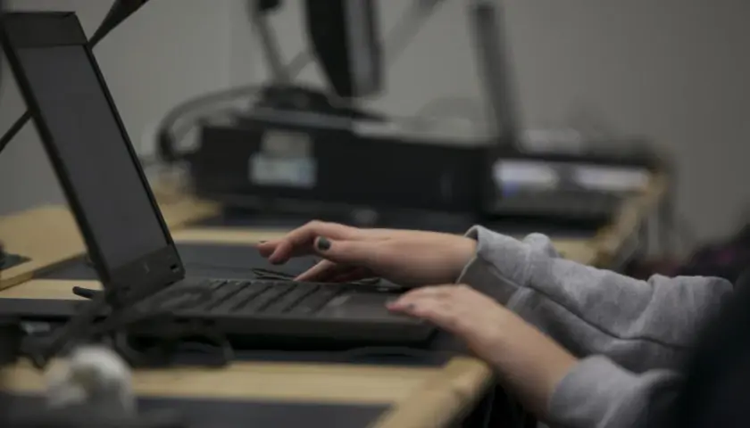 Dłonie piszą na klawiaturze laptopa, jakby śledziły coś w internecie.