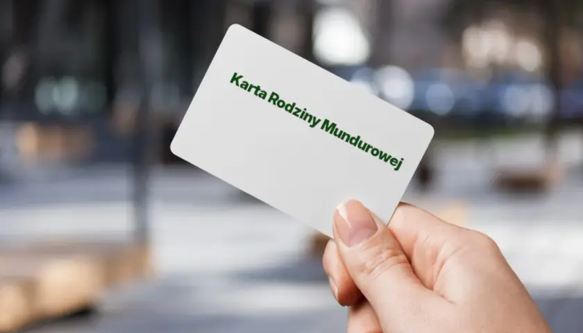 Dłoń trzyma białą kartę z napisem "Karta Rodziny Mundurowej" w kolorze zielonym.