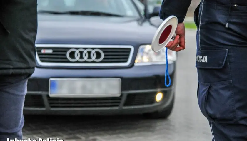 Policjant z Lubuskiej Policji zatrzymuje ruch, trzymając znak stop. Przed nim stoi ciemny samochód Audi.