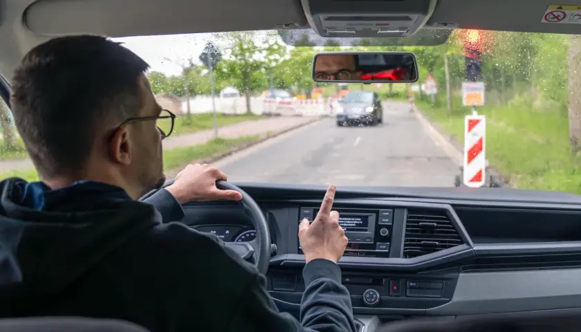 Kierowca w okularach wskazuje palcem na ekran nawigacji, gdy zbliża się do drogi dla pieszych.