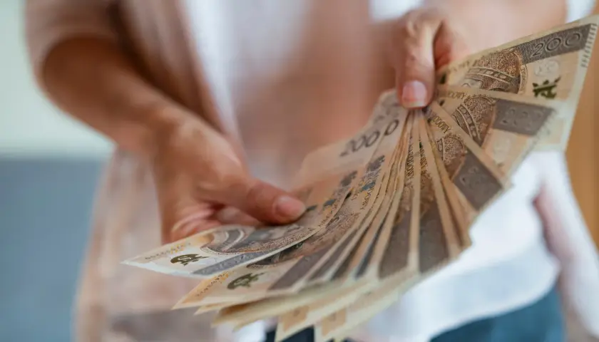 Dłonie trzymają wachlarz banknotów 200 zł. To symbol nagrody jubileuszowej za 40 lat pracy w budżetówce.
