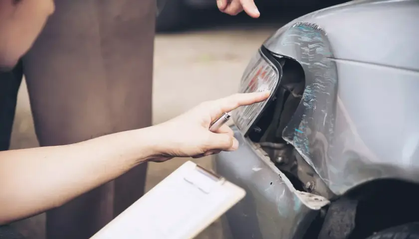 Dwóch mężczyzn ocenia uszkodzenia samochodu po wypadku. Jeden z nich, trzymający dokumenty, wskazuje na zniszczony reflektor. To zdarzenie z pewnością będzie miało wpływ na koszt naprawy, być może nawet przekroczy 288 kk.
