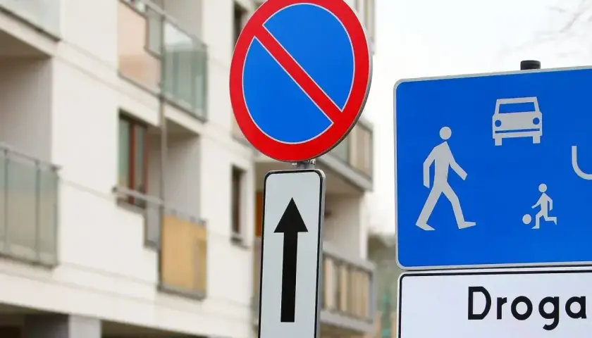 Znak zakaz postoju informuje, że nie można tu parkować. Obok znak drogi wewnętrznej z ikonami pieszych i samochodu.
