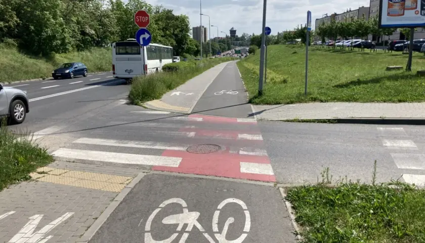 Wyraźna droga dla rowerów z oznakowaniem, obok pasy dla pieszych i jezdnia z autobusem.