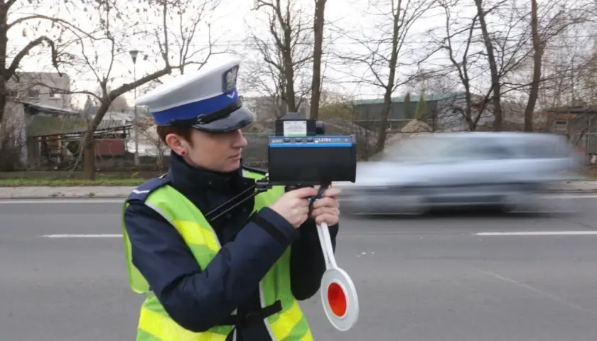 Policjantka w kamizelce odblaskowej mierzy prędkość przejeżdżającego samochodu radarem.