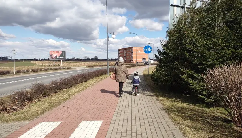 Kobieta z dzieckiem na rowerze idzie chodnikiem. Długość kolumny pieszych nie może przekraczać, ale tu jest tylko dwójka.