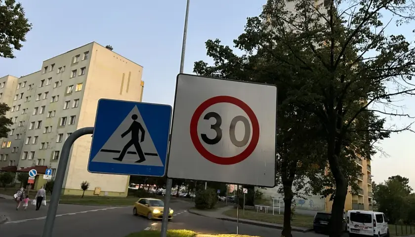 Znak D43 (przejście dla pieszych) i znak ograniczenia prędkości do 30 km/h na tle bloków mieszkalnych i drzew.
