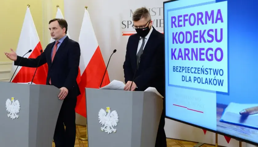 Konferencja prasowa dotycząca reformy kodeksu karnego. Mówcy przy mównicach z godłem Polski, na ekranie hasło "Bezpieczeństwo dla Polaków" i symbole sprawiedliwości.