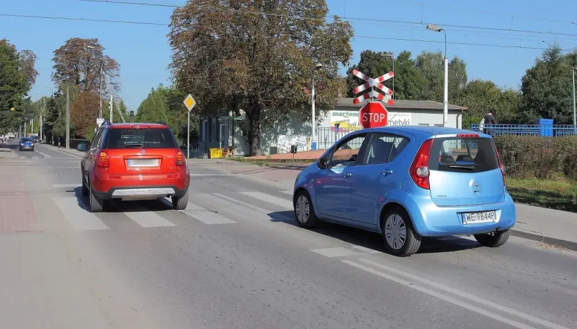 Czerwony i niebieski samochód na przejściu dla pieszych, czerwony czeka na wymijanie, niebieski już rusza.