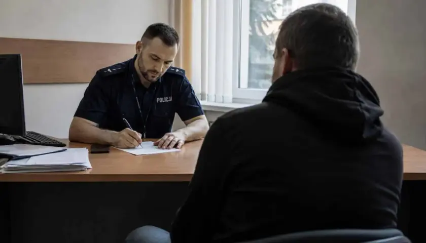 Policjant spisuje zeznania podejrzanego w pokoju przesłuchań.