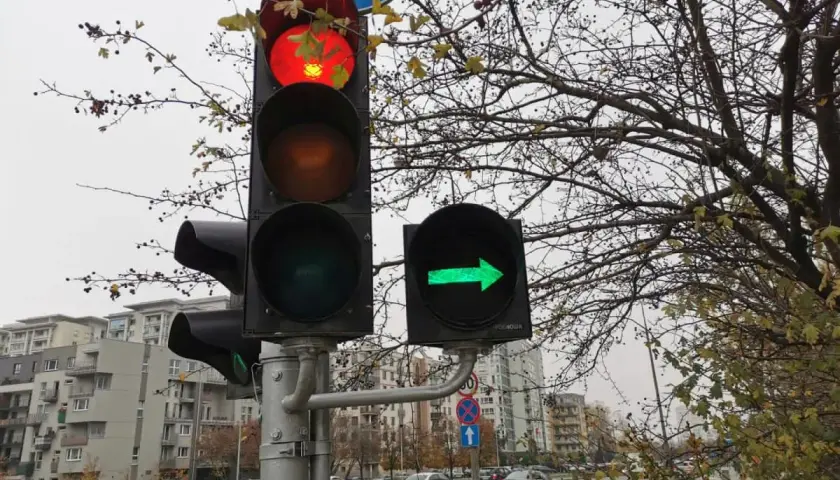 Sygnalizator S2 z czerwonym światłem na górze i zieloną strzałką w prawo. Za nim drzewa i budynki.