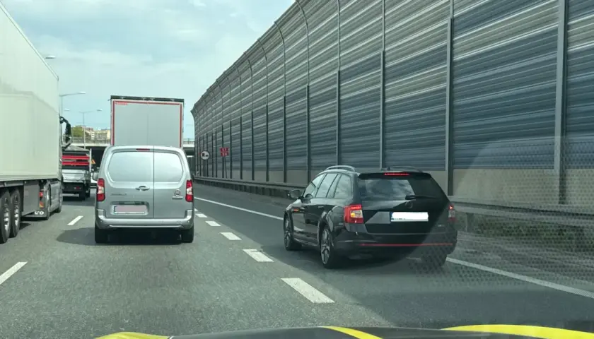 Kork na autostradzie, samochody i ciężarówki stoją w korku. Widać znak informujący o jeździe na suwak.