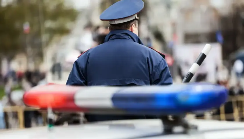 Policjant w mundurze stoi przy radiowozie. Zastanawiasz się, ile zarabia policja kryminalna?