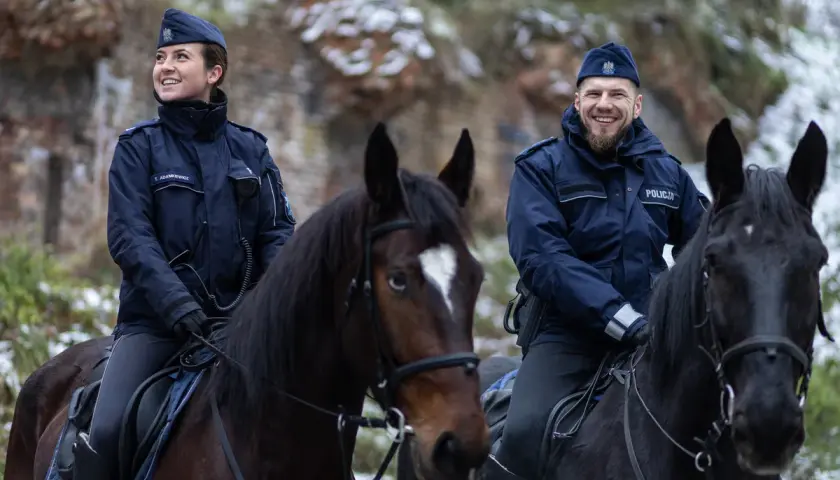 Policjanci na koniach, w tym przełożony, patrolują zimowy teren.