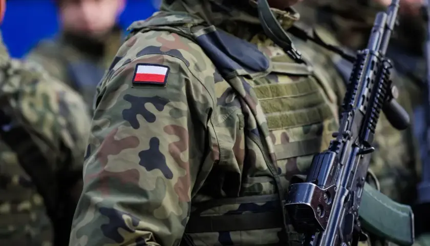 Żołnierze w kamuflażu, z polską flagą na ramieniu, gotowi do mobilizacji. Broń w rękach, czujność na twarzach.