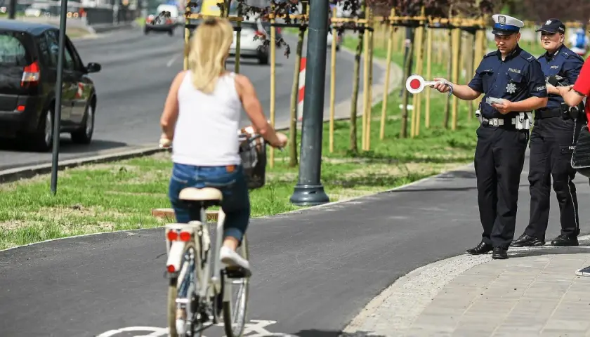 Policjant zatrzymuje kobietę jadącą rowerem po chodniku.