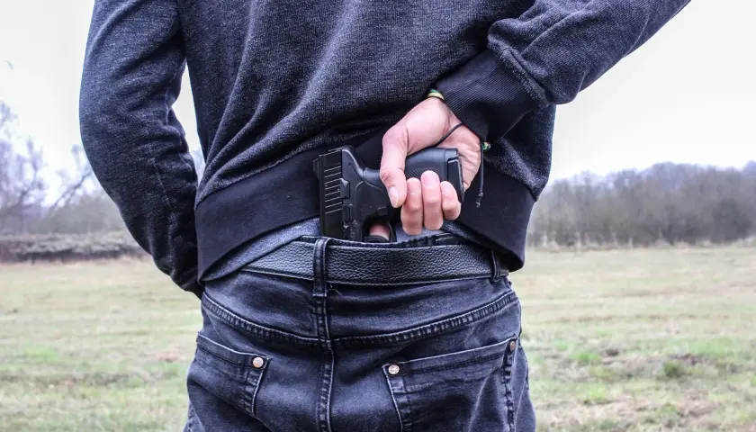 Mężczyzna chowa pistolet za pasem, gotowy do egzekwowania haraczu.