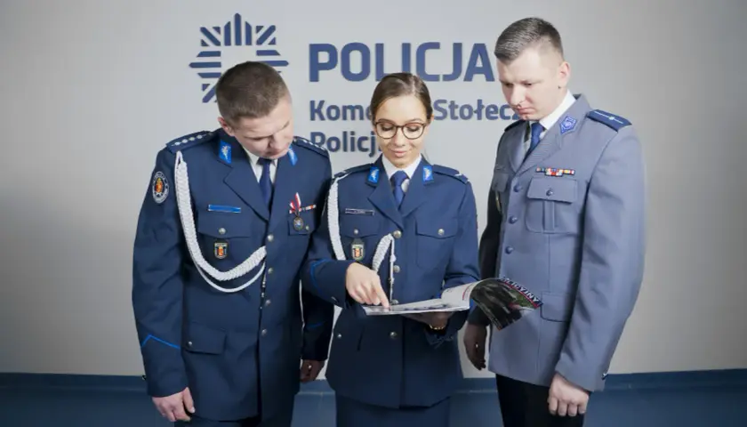 Policjanci w mundurach omawiają materiały. Pokazują, jak nosić furażerkę policja.