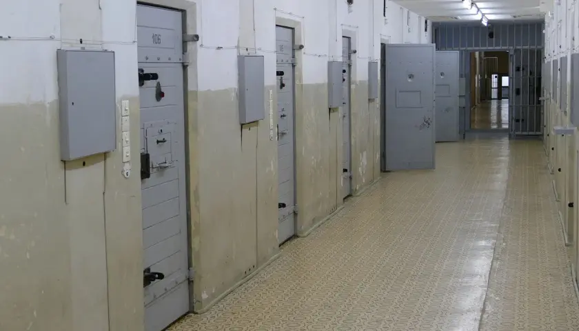Korytarz więzienny z celami po obu stronach. Na drzwiach jednej z cel widnieje numer 106. W tle kraty i kolejne drzwi.