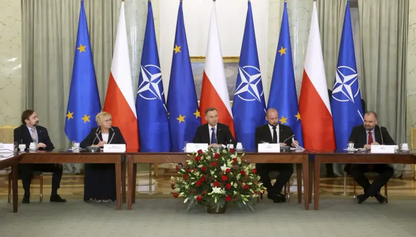 Spotkanie przy stole z flagami Polski, UE i NATO. Dyskusja o bezpieczeństwie i artykuł 5 NATO.