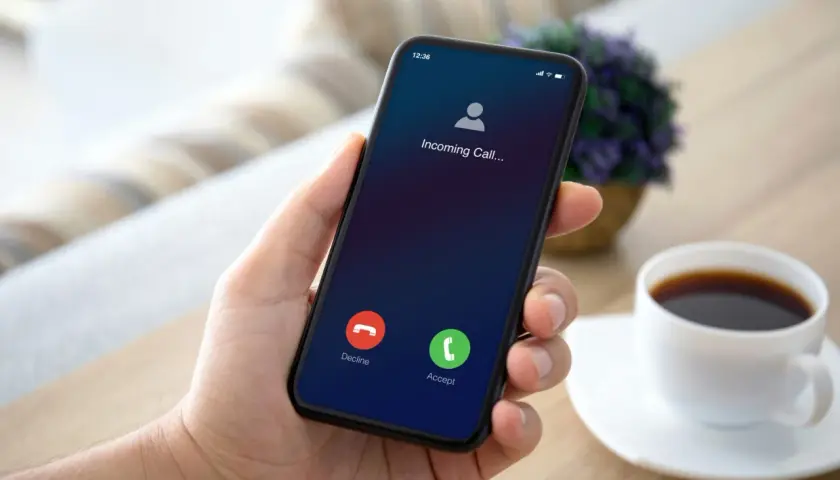 Dłoń trzyma smartfon z ekranem połączenia przychodzącego.