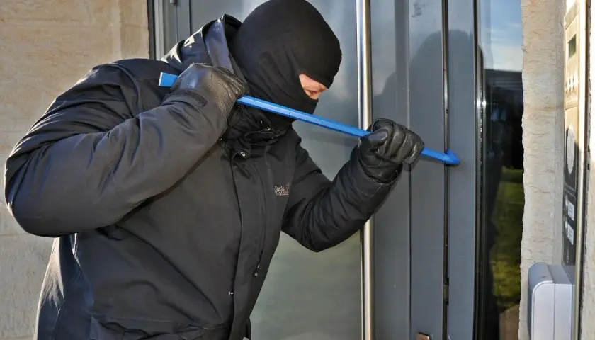 Złodziej w kominiarce i rękawiczkach próbuje wyważyć drzwi łomem. To może być próba włamania, zgodnie z art. 279 kk.